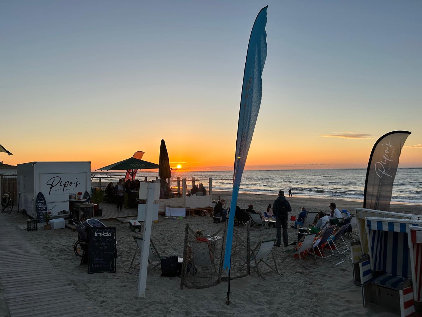 Die Terrasse am Abend: Beachflags, Liegestühle, Sonnenuntergang